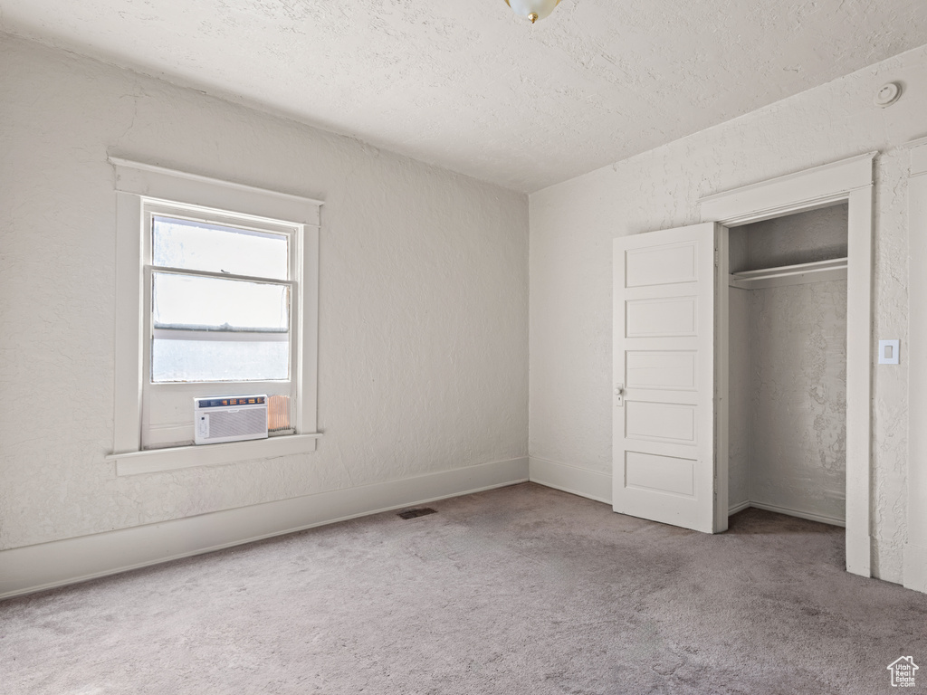 Unfurnished bedroom with carpet floors, cooling unit, a textured ceiling, and a closet