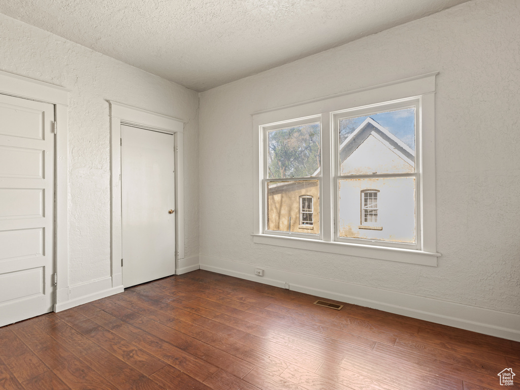 Unfurnished bedroom featuring dark wood-type flooring, baseboards, a textured ceiling, and a textured wall