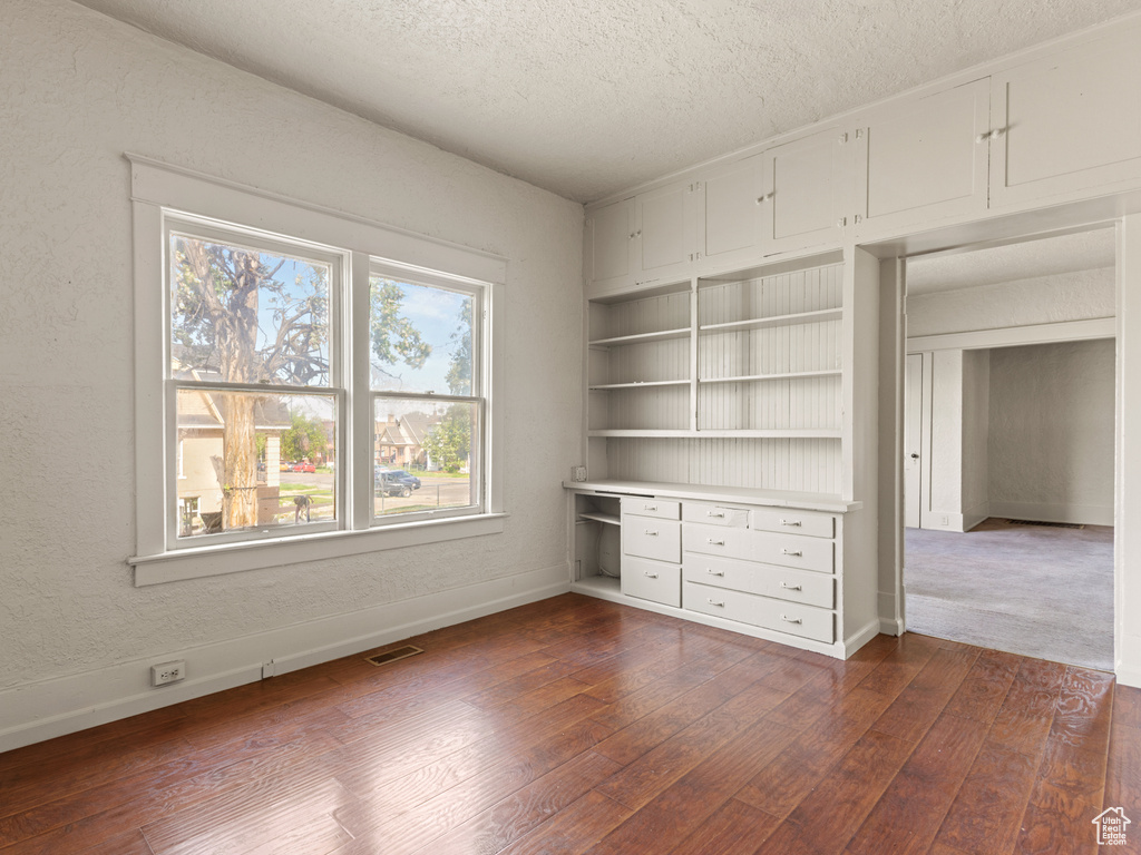 Unfurnished bedroom featuring a textured ceiling, dark wood-type flooring, and baseboards