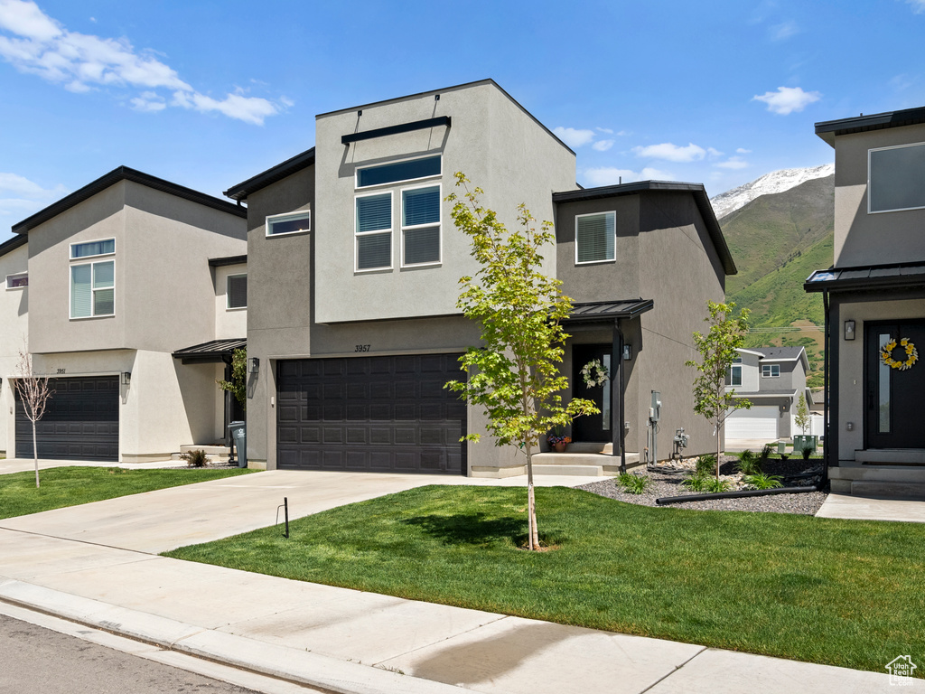 Contemporary home with a garage, stucco siding, a mountain view, a front yard, and driveway