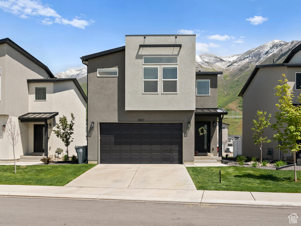 Modern home with a standing seam roof, concrete driveway, a garage, stucco siding, and a front lawn