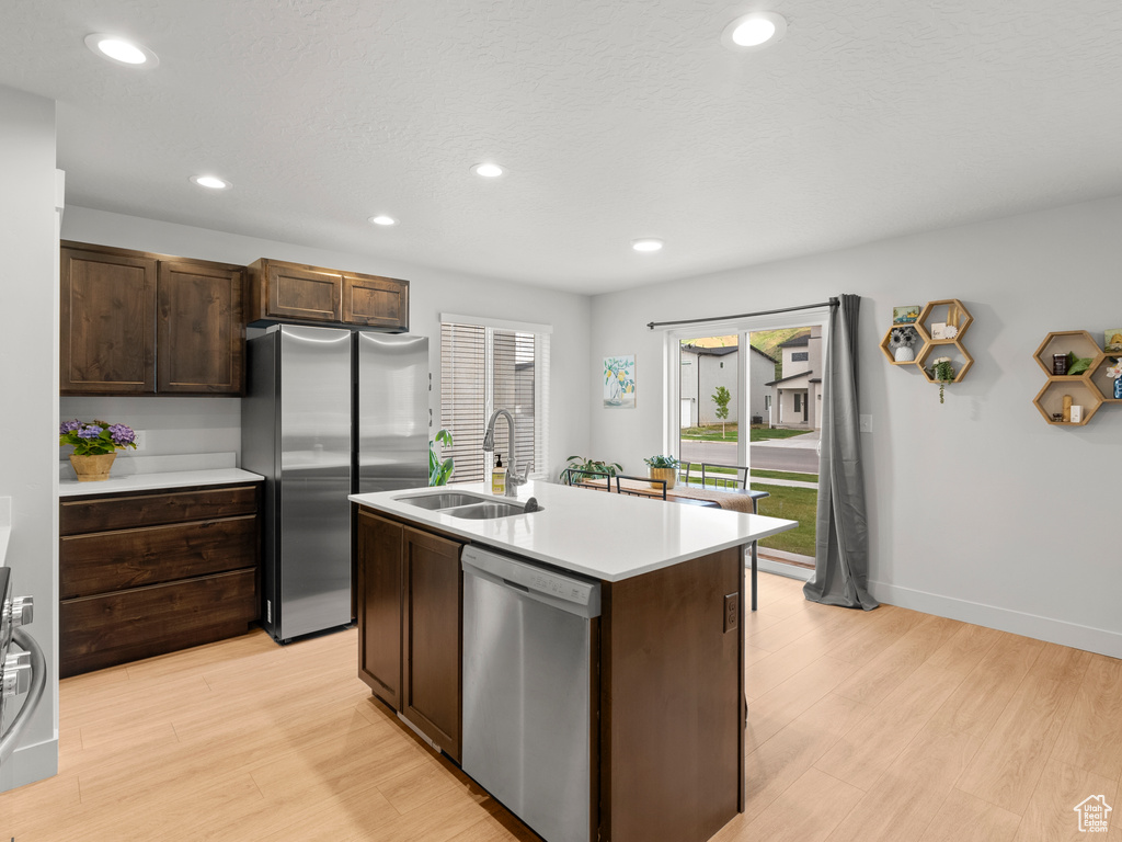 Kitchen with appliances with stainless steel finishes, a sink, light wood-type flooring, dark brown cabinetry, and recessed lighting