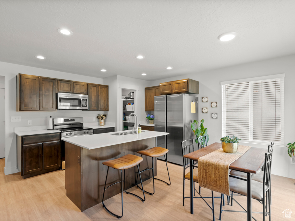 Kitchen featuring appliances with stainless steel finishes, a sink, light wood-style flooring, a kitchen bar, and recessed lighting