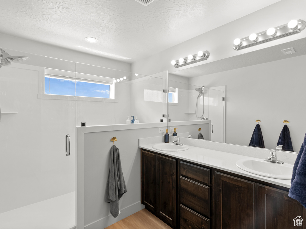 Full bathroom featuring a stall shower, double vanity, a textured ceiling, and wood finished floors