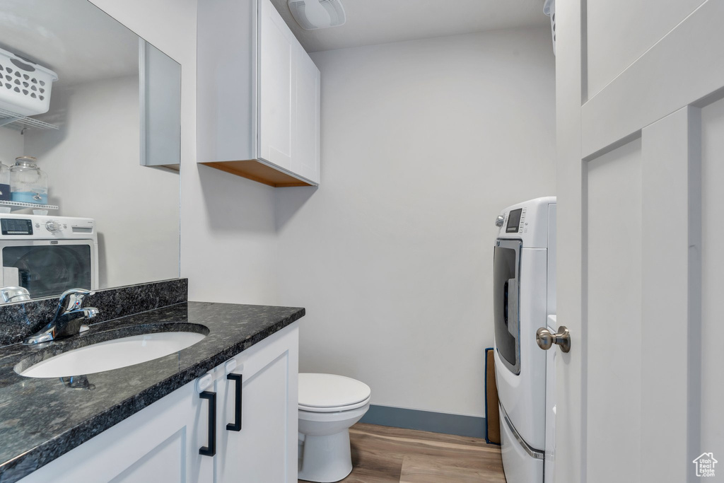 Half bath featuring washer / dryer, wood finished floors, vanity, toilet, and baseboards