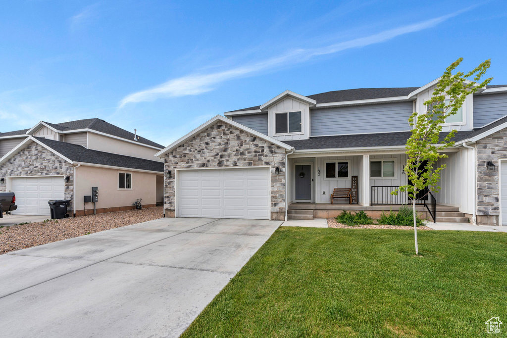 View of front of home with stone siding, a porch, an attached garage, driveway, and a front yard