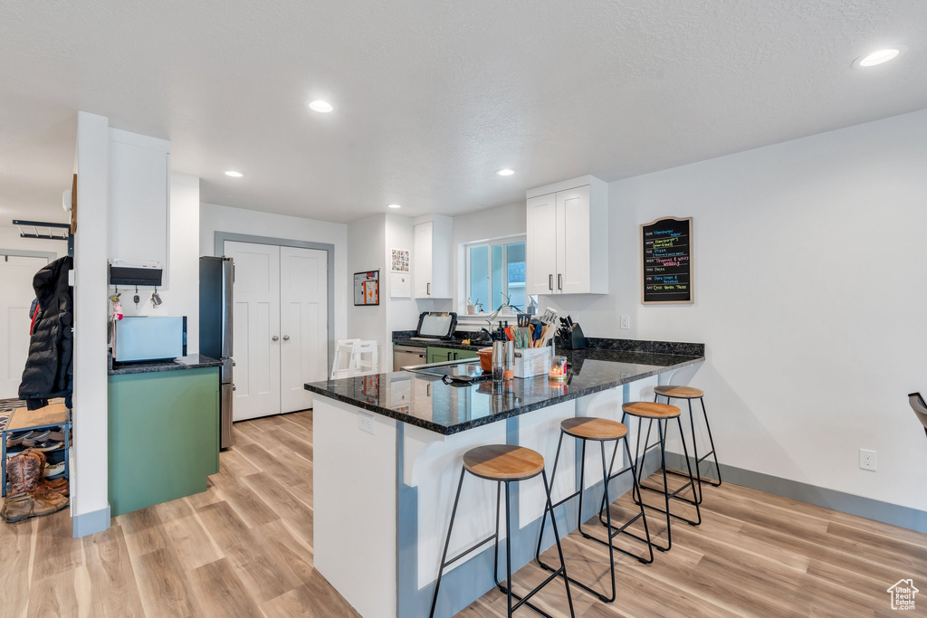 Kitchen with a peninsula, a breakfast bar area, white cabinetry, light wood-style floors, and recessed lighting