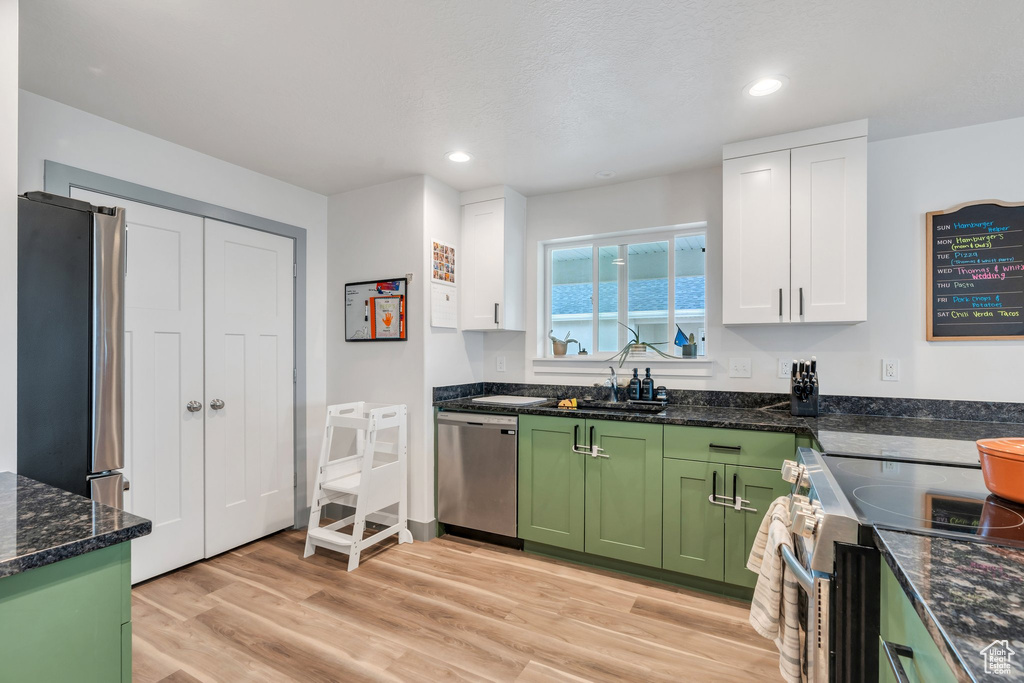 Kitchen featuring green cabinets, stainless steel appliances, a sink, white cabinets, and light wood finished floors