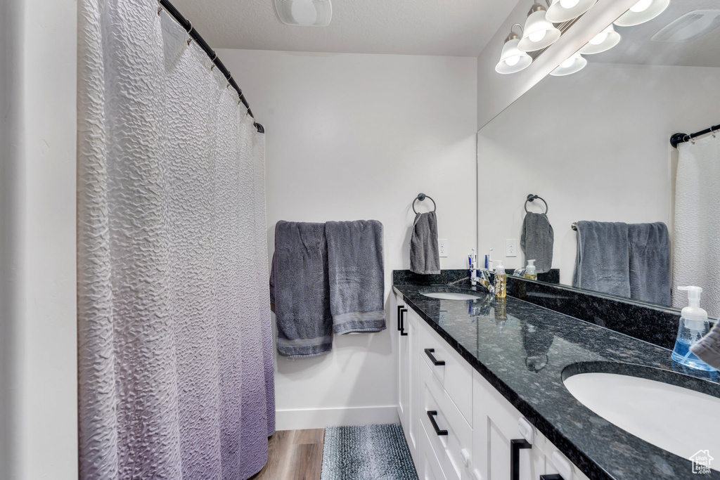 Bathroom with double vanity, baseboards, and wood finished floors