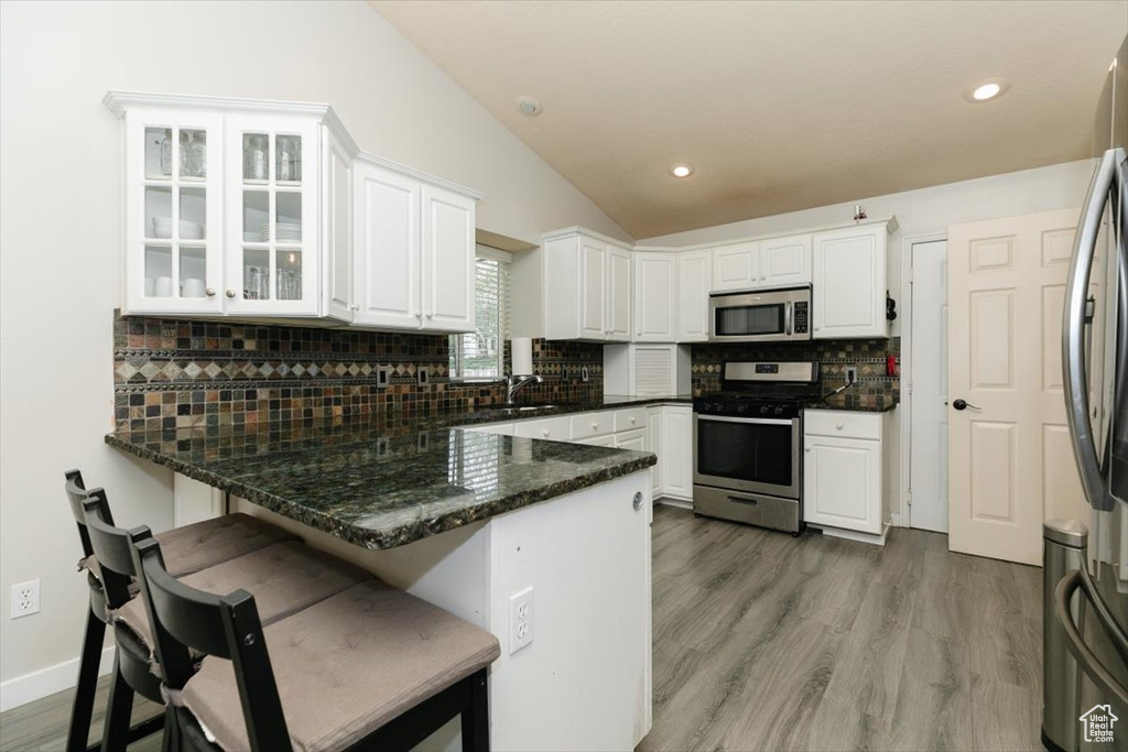 Kitchen with appliances with stainless steel finishes, a peninsula, lofted ceiling, white cabinetry, and a sink