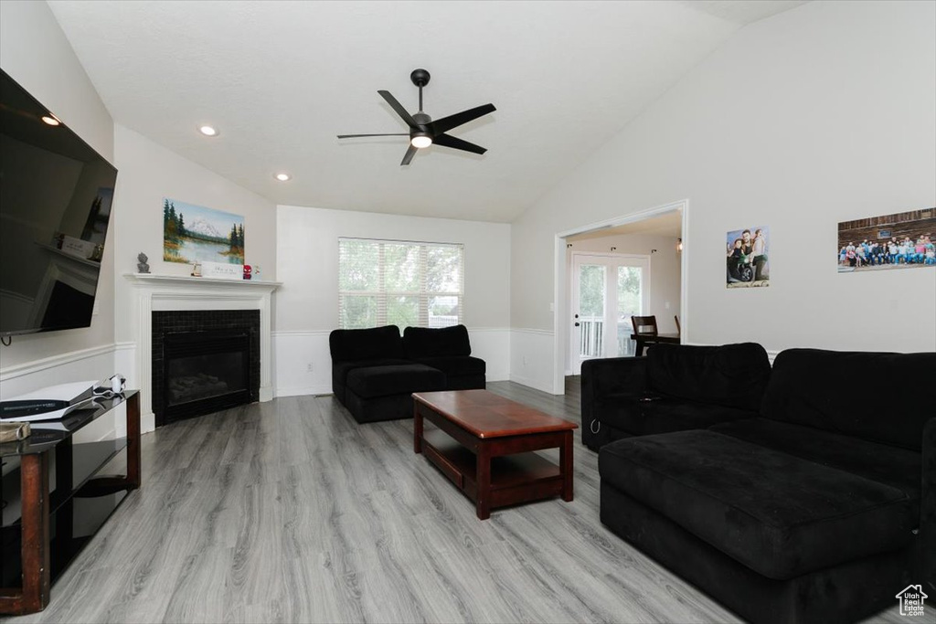 Living area with vaulted ceiling, ceiling fan, a wainscoted wall, light wood-style floors, and a glass covered fireplace
