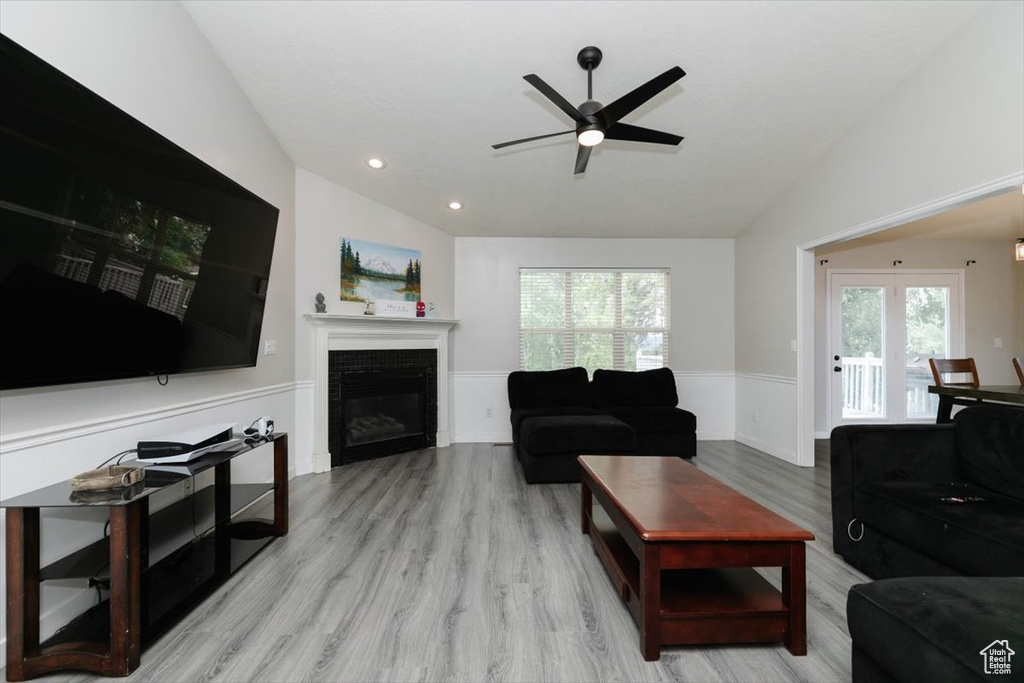 Living area with ceiling fan, a wainscoted wall, lofted ceiling, wood finished floors, and a glass covered fireplace