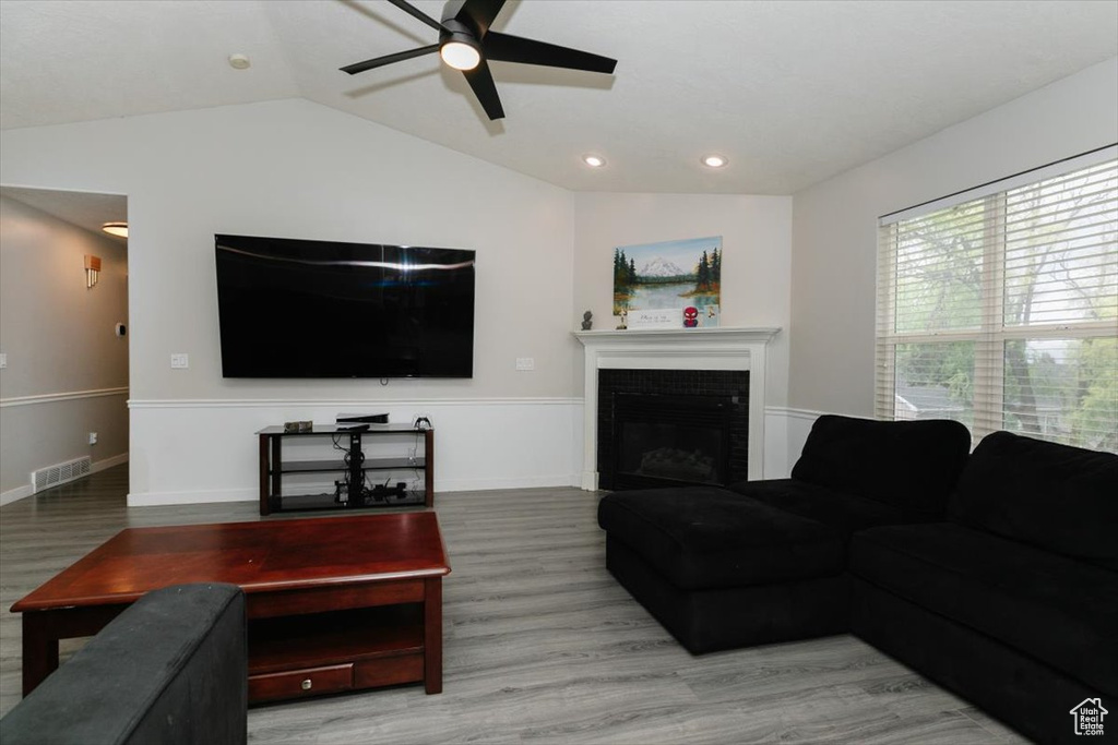 Living area featuring a ceiling fan, lofted ceiling, wood finished floors, a tiled fireplace, and recessed lighting