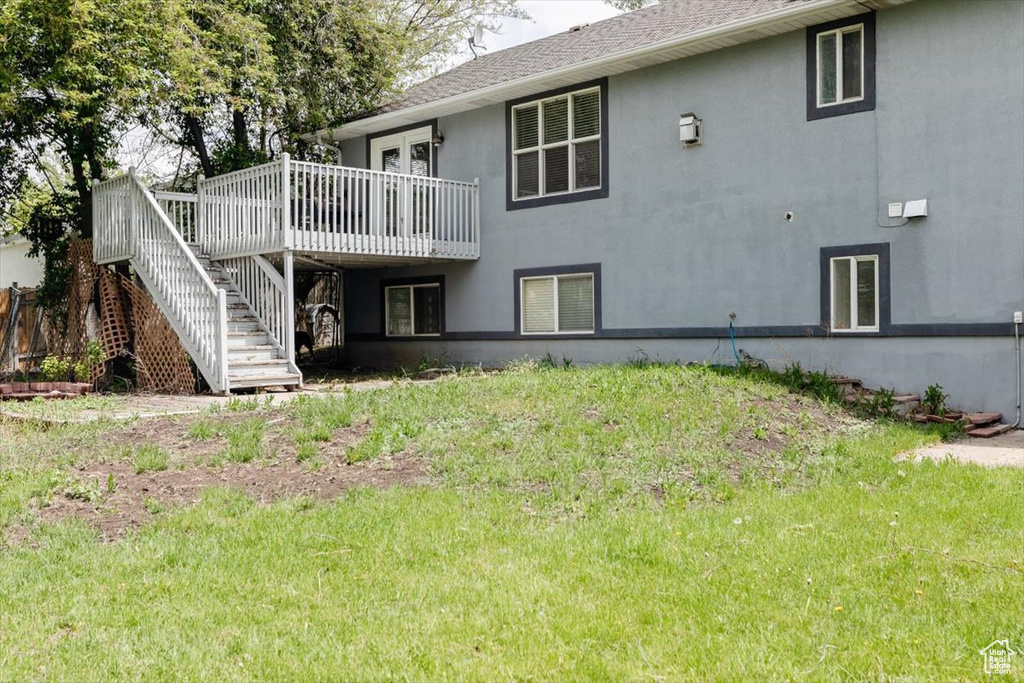 Back of property featuring a deck, stairway, stucco siding, and a yard