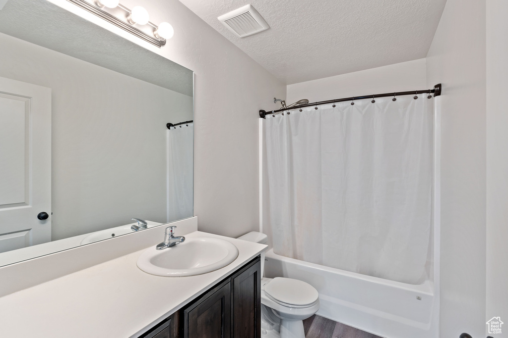 Full bath with a textured ceiling, toilet, shower / tub combo with curtain, vanity, and wood finished floors