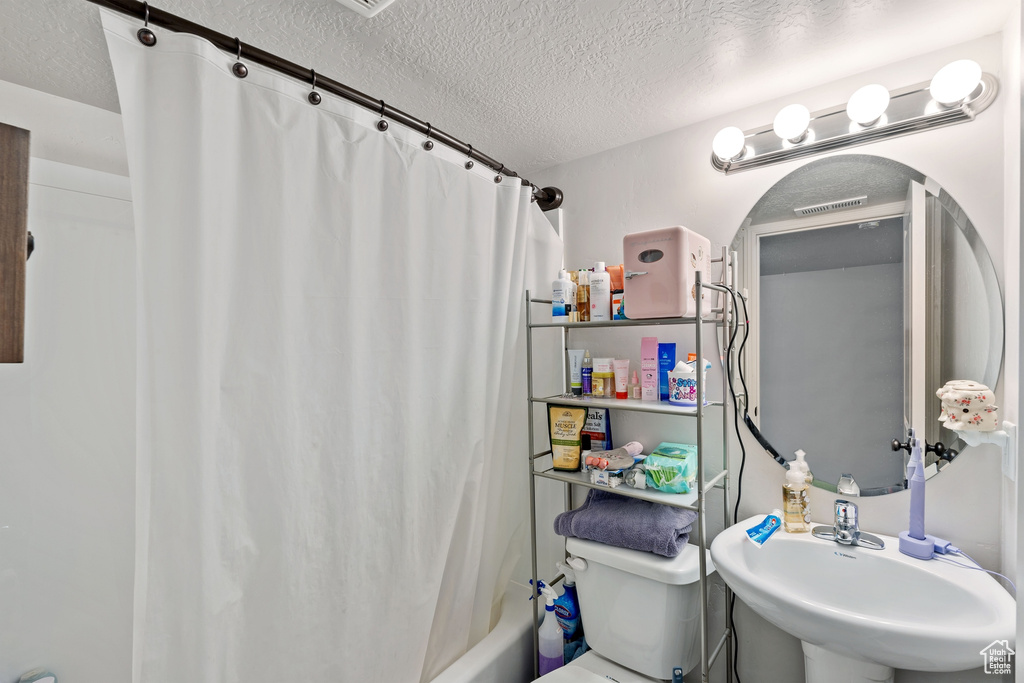 Full bath featuring a textured ceiling, a sink, shower / bath combo with shower curtain, and toilet