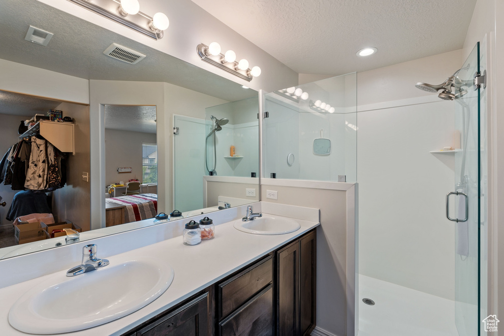 Full bathroom with ensuite bath, a stall shower, a textured ceiling, and double vanity