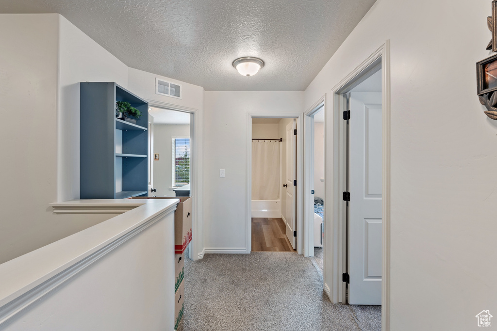 Hallway with a textured ceiling, light colored carpet, and baseboards