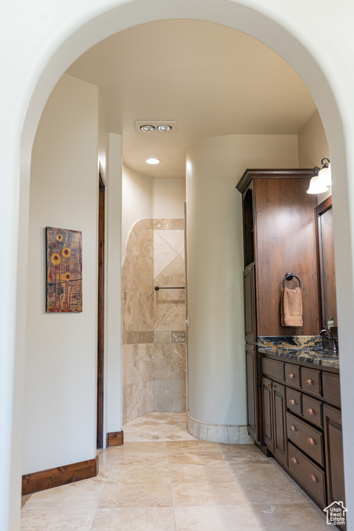 Full bath featuring baseboards, double vanity, tiled shower, and recessed lighting