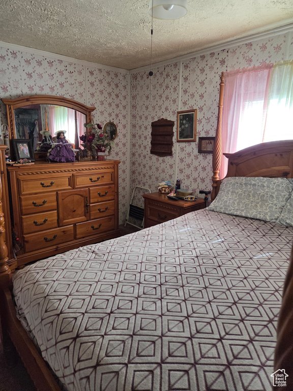 Bedroom with wallpapered walls, a textured ceiling, and ornamental molding