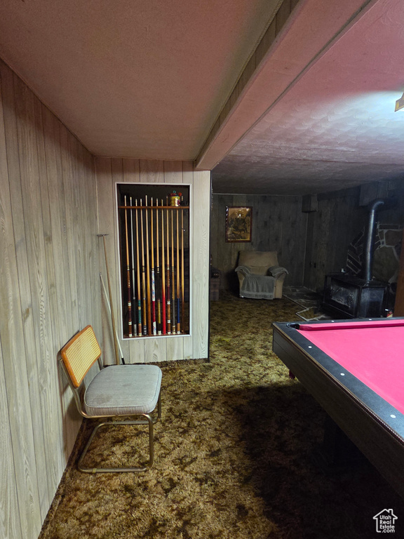 Recreation room with a wood stove, wood walls, carpet flooring, and a textured ceiling