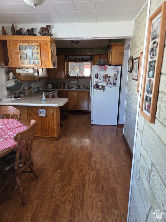 Kitchen with freestanding refrigerator, a peninsula, electric range oven, brown cabinets, and dark wood-style floors