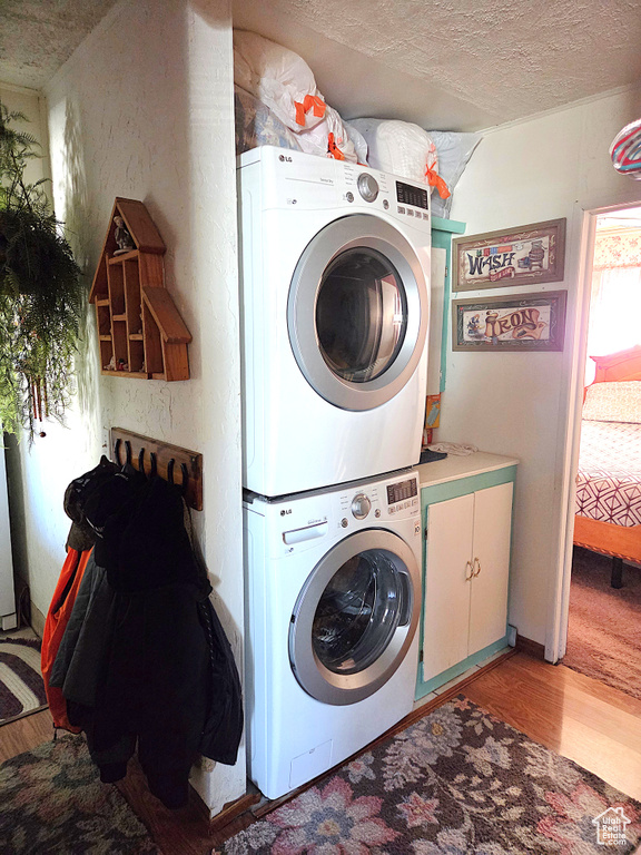 Laundry room with stacked washer / drying machine, cabinet space, light wood-style flooring, and a textured ceiling