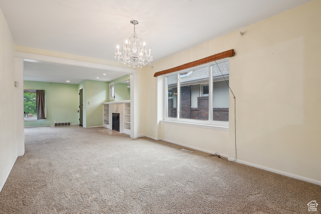 Unfurnished living room with carpet floors, a chandelier, baseboards, and a fireplace with flush hearth