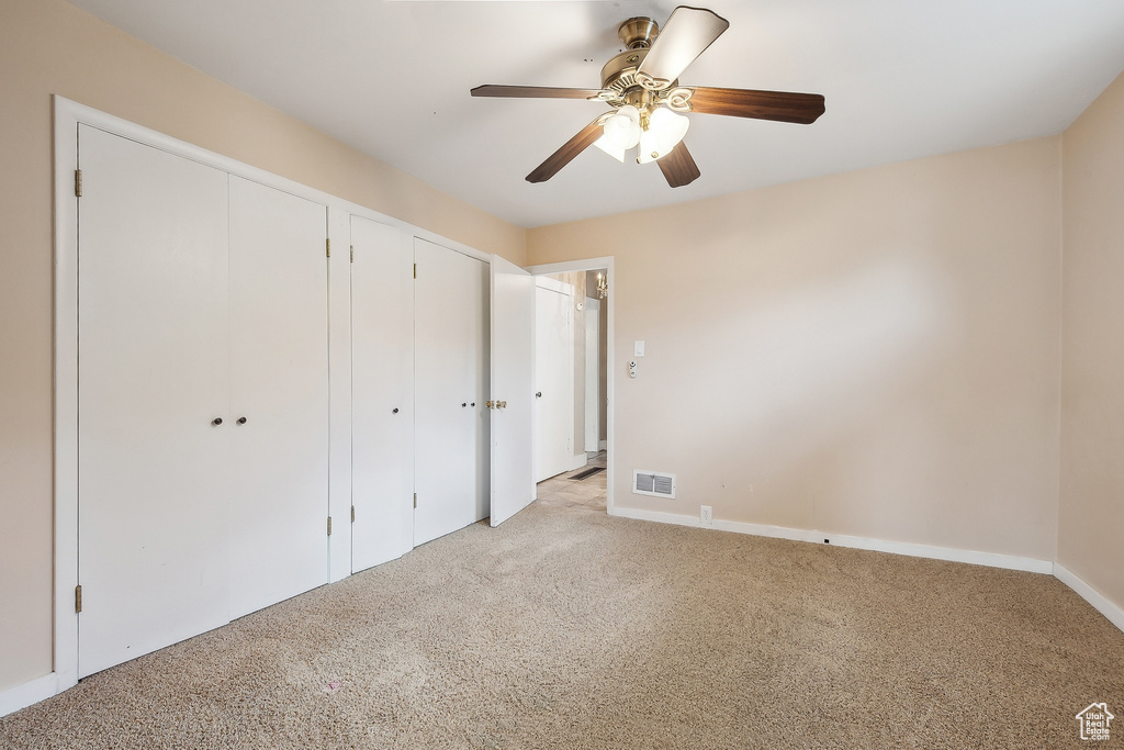 Unfurnished bedroom with light colored carpet, multiple closets, baseboards, and a ceiling fan