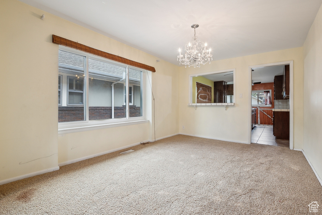 Empty room with carpet, a chandelier, and baseboards