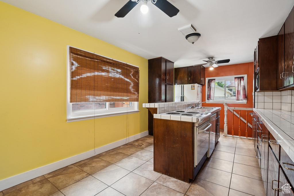 Kitchen featuring tile countertops, a ceiling fan, dark brown cabinets, and an island with sink