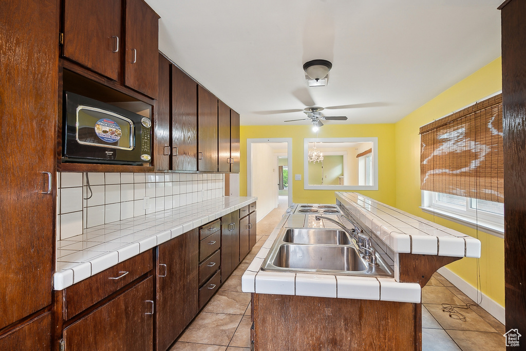 Kitchen with tile countertops, a sink, a kitchen island with sink, light tile patterned flooring, and a ceiling fan