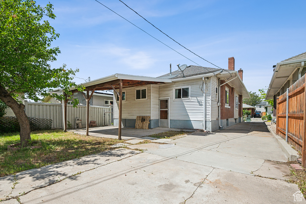 Rear view of house featuring fence, a chimney, driveway, and an attached carport