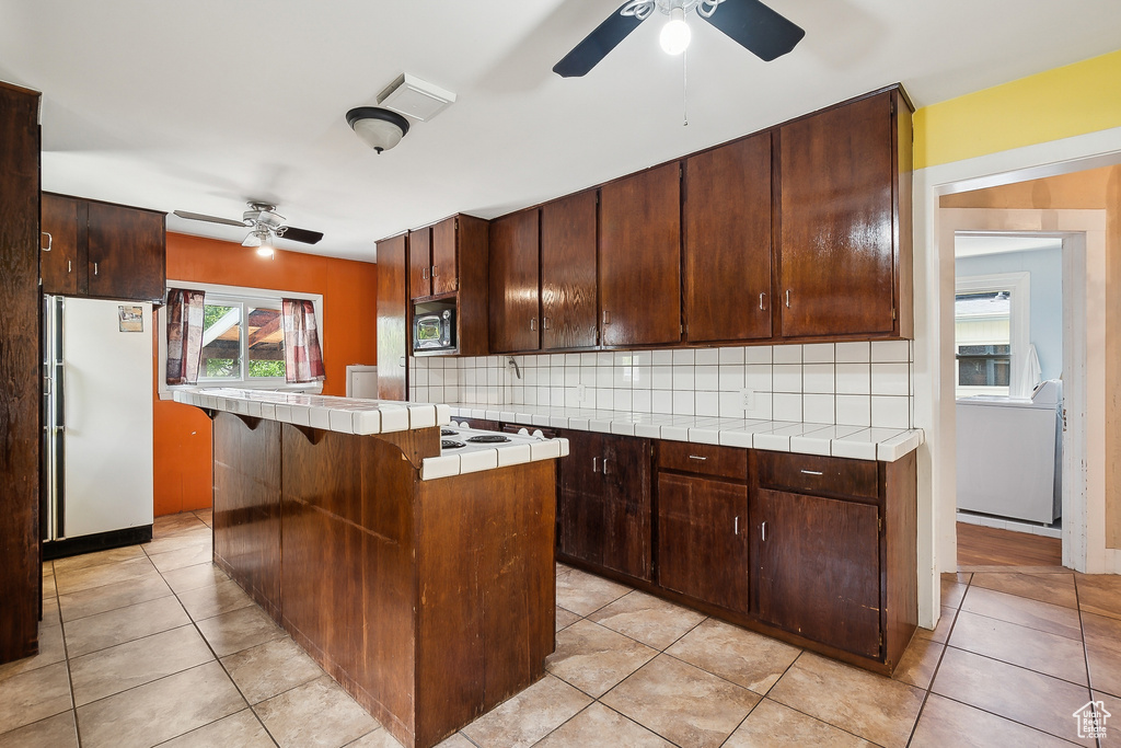 Kitchen with a ceiling fan, freestanding refrigerator, stainless steel microwave, tile countertops, and backsplash