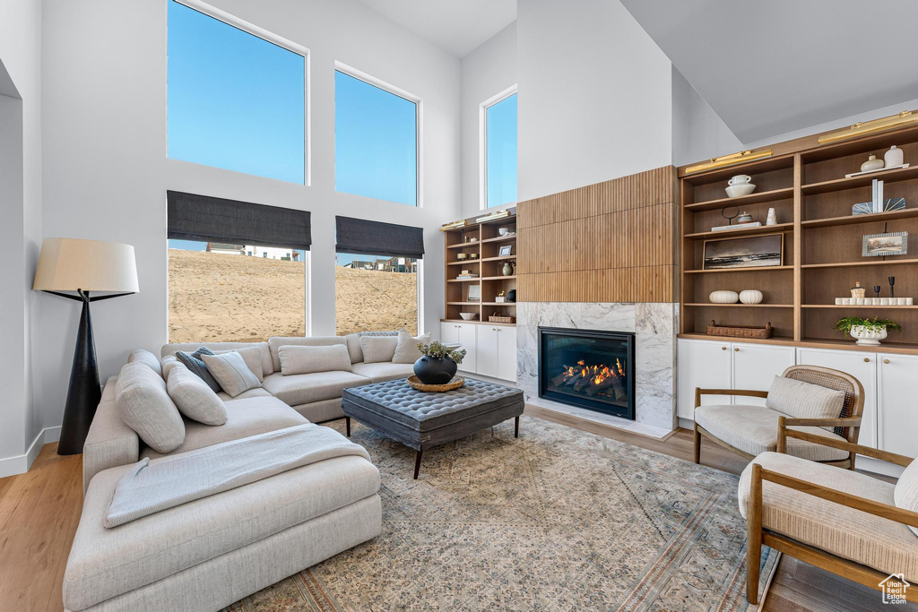 Living room with a high ceiling, light wood-type flooring, a high end fireplace, and baseboards