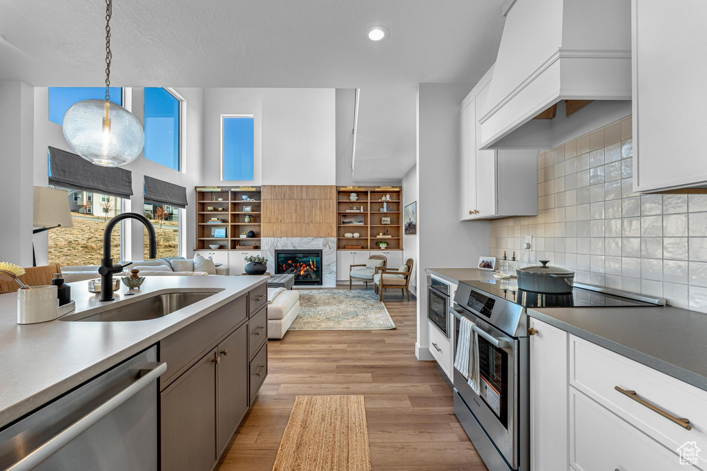 Kitchen featuring appliances with stainless steel finishes, a sink, custom exhaust hood, a fireplace, and decorative backsplash