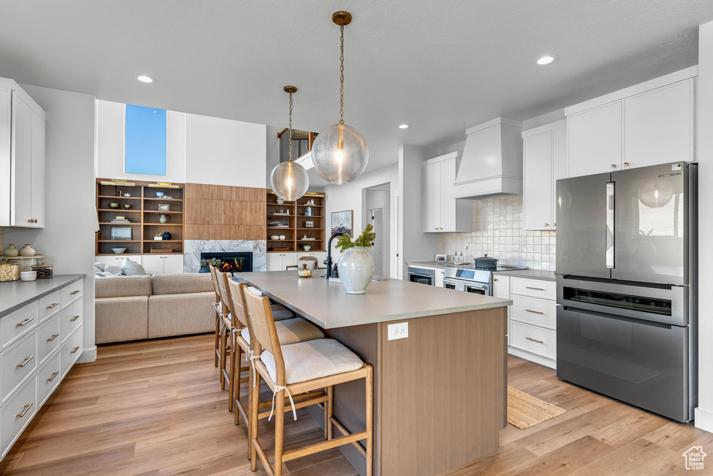Kitchen with stainless steel appliances, custom exhaust hood, light wood-style flooring, a glass covered fireplace, and recessed lighting