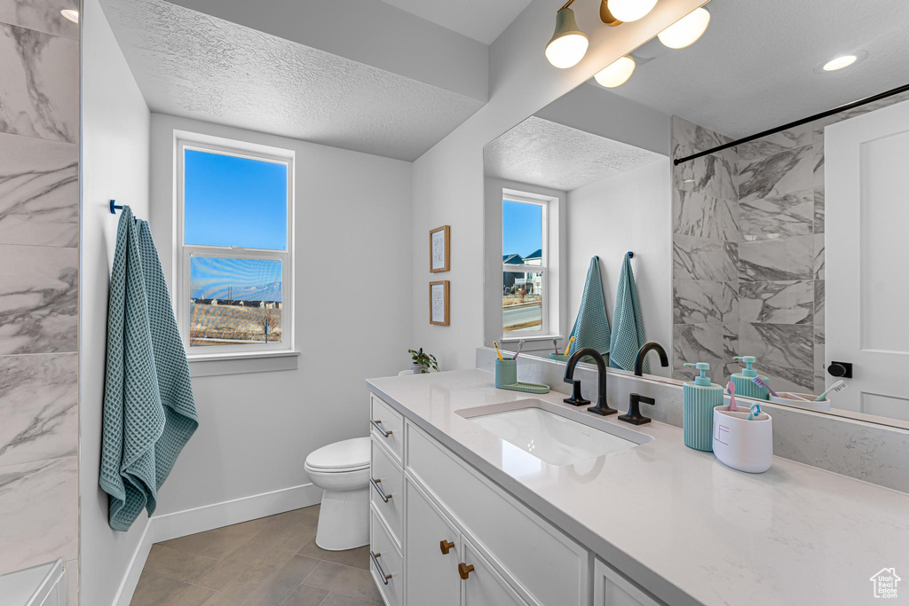 Full bathroom with a textured ceiling, baseboards, vanity, a shower, and toilet