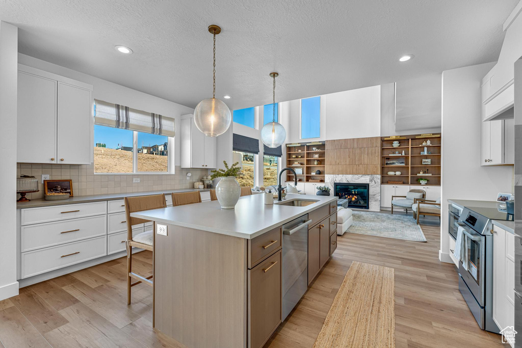 Kitchen featuring appliances with stainless steel finishes, a sink, a kitchen island with sink, white cabinets, and recessed lighting