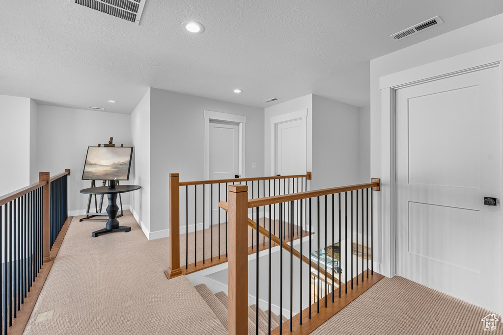 Hallway featuring an upstairs landing, light colored carpet, baseboards, recessed lighting, and a textured ceiling