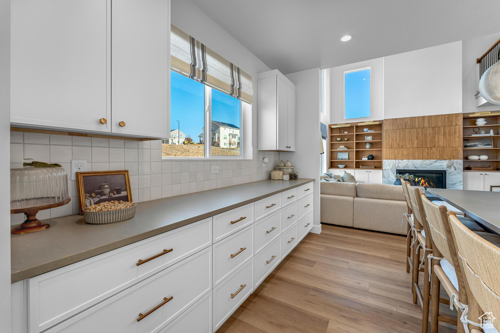 Kitchen with light wood finished floors, a glass covered fireplace, tasteful backsplash, white cabinets, and recessed lighting