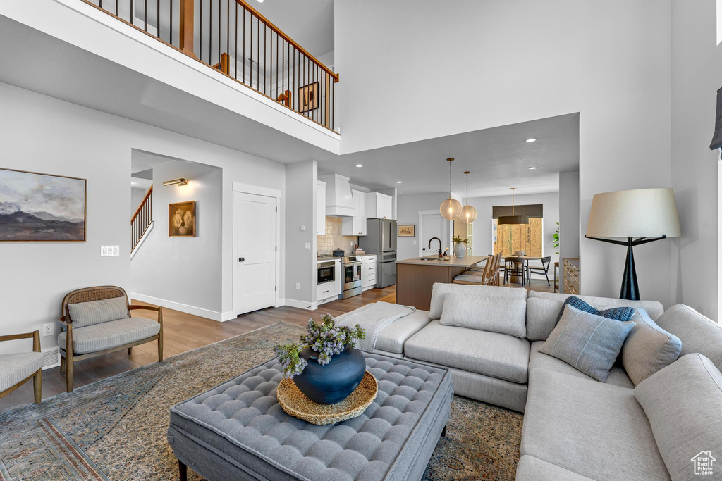 Living area with dark wood-style flooring, a towering ceiling, baseboards, stairs, and recessed lighting