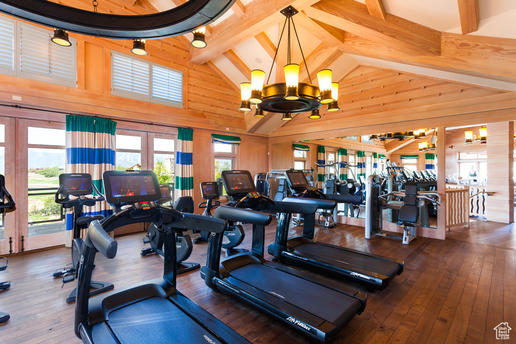 Gym featuring wooden walls, hardwood / wood-style flooring, a chandelier, beam ceiling, and high vaulted ceiling