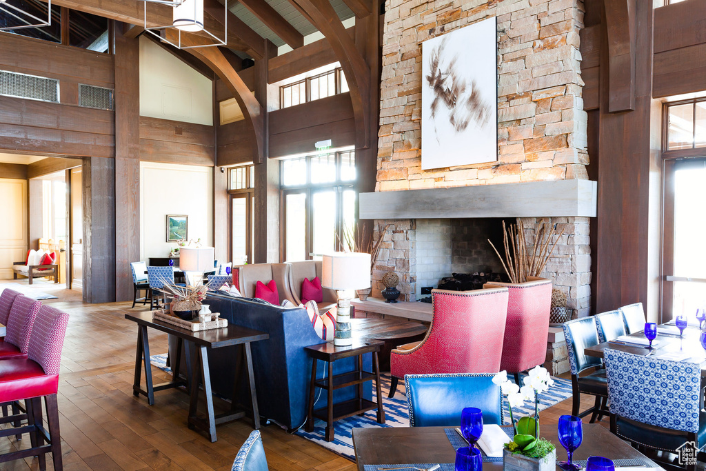 Living area with plenty of natural light, a stone fireplace, hardwood / wood-style floors, high vaulted ceiling, and beam ceiling