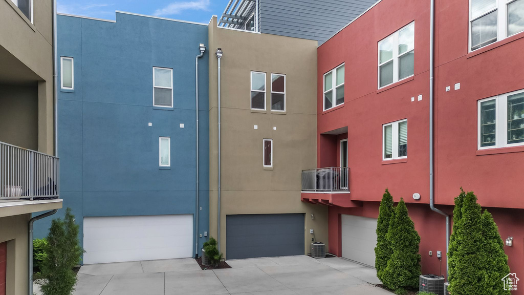 View of building exterior featuring an attached garage, driveway, and central AC