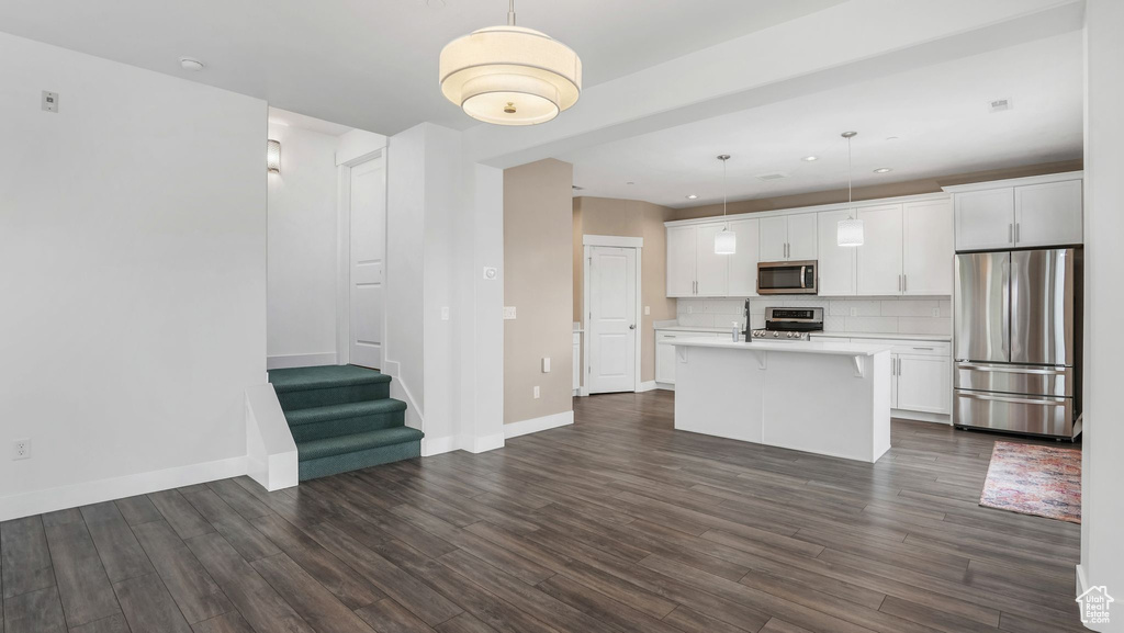 Kitchen featuring stainless steel appliances, light countertops, dark wood-style flooring, white cabinetry, and an island with sink