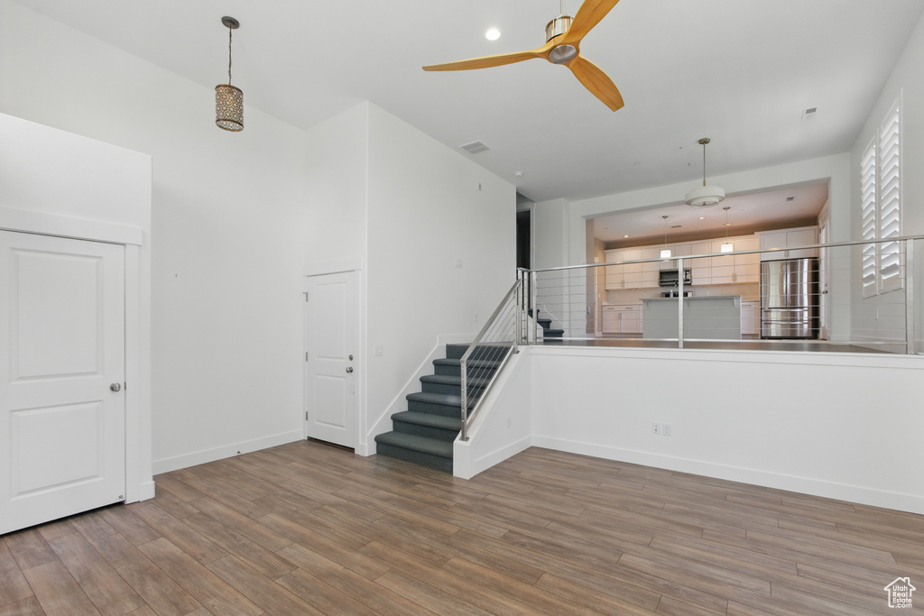 Unfurnished living room with ceiling fan, wood finished floors, baseboards, and stairway