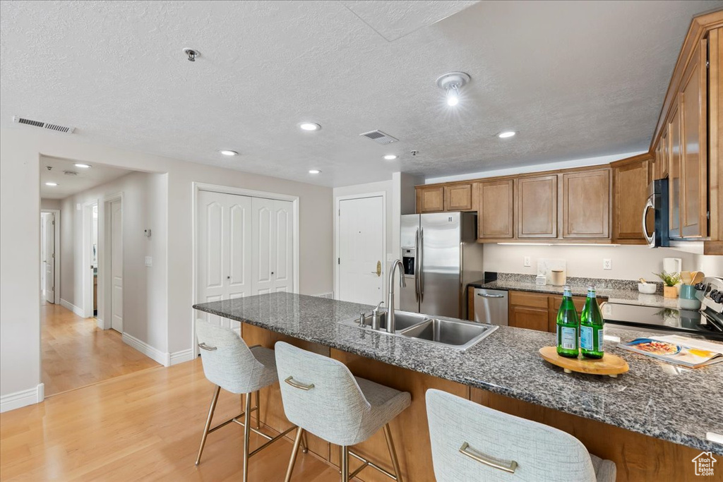 Kitchen featuring appliances with stainless steel finishes, brown cabinetry, a breakfast bar area, a sink, and light wood-type flooring