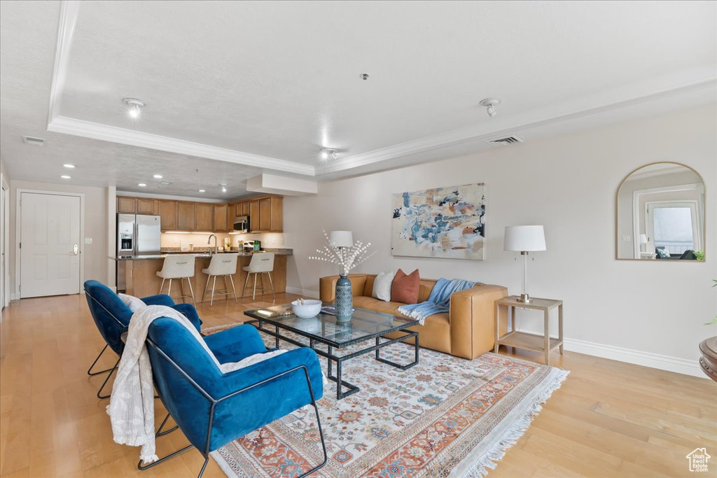 Living area with a raised ceiling, light wood-type flooring, recessed lighting, baseboards, and ornamental molding