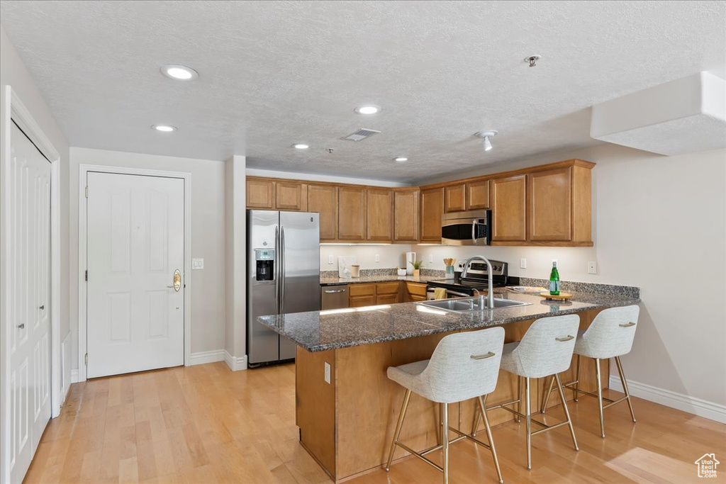 Kitchen with appliances with stainless steel finishes, brown cabinetry, a peninsula, a sink, and baseboards